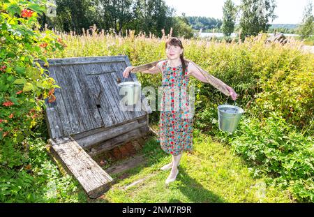 Attraktive Frau in der Nähe des Dorfes hölzernes Wasser am sonnigen Sommertag Stockfoto