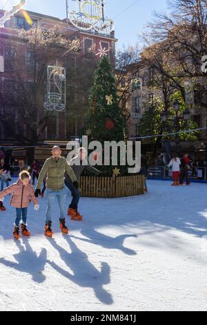 Granada, Spanien; 18. Dezember 2022: Schlittschuhlaufen von Erwachsenen und Kindern auf einer Eisbahn neben einem Weihnachtsbaum an einem sonnigen Wintermorgen in Granada (Spanien) Stockfoto