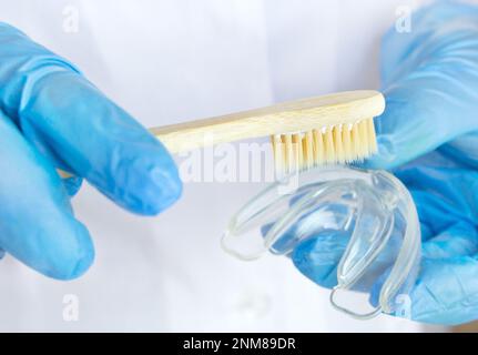 Zahnarztfütterung. Mundschutz mit hölzerner Zahnbürste in den Händen von Ärzten in blauen Handschuhen, Teenager-Kieferorthopädie, Clear Aligner Dental Night Guard ora Stockfoto