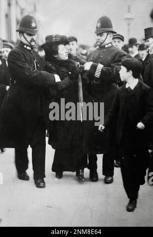 Zwei stürmische Londoner Bobbies verhaften einen Suffragetten. Ein kleiner Junge sieht zu - 1910-1915 Stockfoto