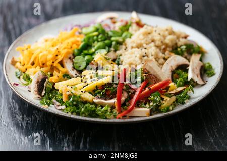 Hausgemachter asiatischer Grünkohl-Salat mit Quinoa, Karotten, Fava-Bohnen, Paprika, Babykorn, Pilze und geräucherter Tofu Stockfoto