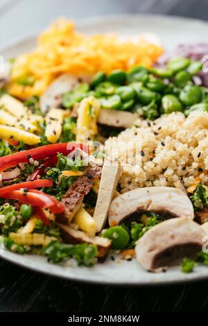 Hausgemachter asiatischer Grünkohl-Salat mit Quinoa, Karotten, Fava-Bohnen, Paprika, Babykorn, Pilze und geräucherter Tofu Stockfoto