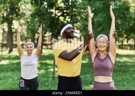 Porträt eines lächelnden Sporttrainers, der eine aktive Seniorin beim Outdoor-Workout unterstützt Stockfoto
