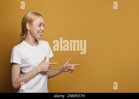 Eine glückliche lächelnde Frau, die Punkte in der rechten Ecke hat, einen freundlichen Gesichtsausdruck hat, trägt ein legeres weißes T-Shirt isoliert auf gelbem Hintergrund Stockfoto