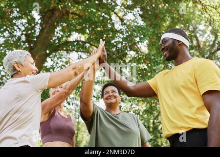 Niedriger Blickwinkel in einer Gruppe aktiver Seniorinnen, High Five mit männlichem Trainer nach einem Outdoor-Workout Stockfoto