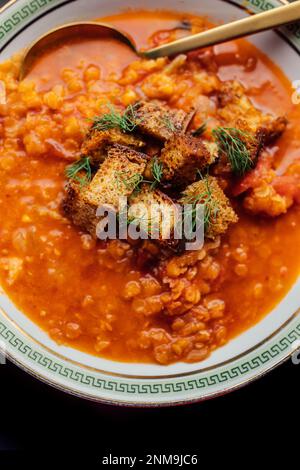 Rote Linsen- und Tomatensuppe mit Fenchel und Croutons in weißer Schüssel mit grünem griechischen Schlüssel und goldenem Löffel Stockfoto