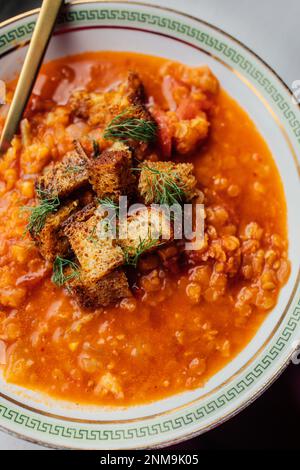 Rote Linsen- und Tomatensuppe mit Fenchel und Croutons in weißer Schüssel mit grünem griechischen Schlüssel und goldenem Löffel Stockfoto