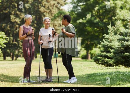 Porträt von aktiven Seniorinnen mit Wanderstöcken, die sich im Freien unterhalten und lächeln Stockfoto