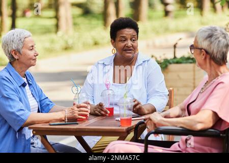 Vielfältige Gruppe von Seniorinnen, die Drinks im Café im Freien genießen und sich unterhalten Stockfoto
