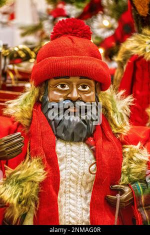 Dunkel gehäutete weihnachtsmann-Puppe aus Holz mit schwarzem Bart, Pullover mit Zopfmuster, roter Strumpfkappe und Mantel mit Fell Stockfoto
