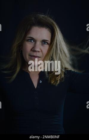 Porträt einer schönen, lächelnden blonden Frau, die ihr Haar mit der Hand in Bewegung hält Stockfoto
