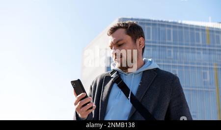 Ein Mann stand wieder draußen im Stadtgebäude und schaute auf sein Handy. Stockfoto