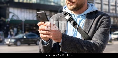Mobiltelefon in den Händen eines Mannes, männlicher Mensch, der auf der Straße in der Stadt steht und sein Telefon benutzt. Stockfoto