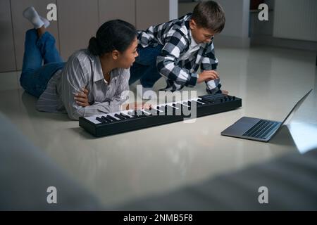 Mama hilft dem Sohn beim Online-Lernen zum digitalen Klavier Stockfoto