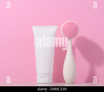 Weißer Kunststoffschlauch und eine Massagebürste zur Gesichtsreinigung auf pinkfarbenem Hintergrund, Artikel für kosmetische Verfahren Stockfoto