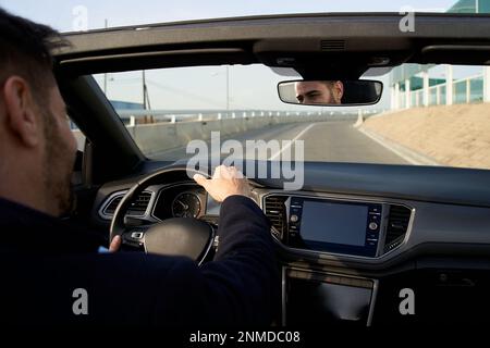 Ein Mann mittleren Alters, der ein Cabrio auf der Stadtstraße fährt. Männlicher Erwachsener genießt das Urlaubsgefühl der Freiheit Stockfoto