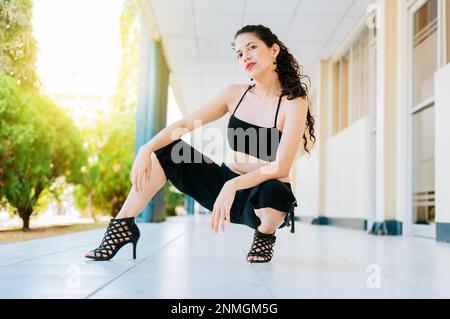 Porträt einer Tänzerin mit Absätzen auf dem Boden, die in die Kamera schaut. Portrait eines Tanzmädchens in High Heels, das sich auf dem Boden hockt, Tanzkünstlerin Stockfoto