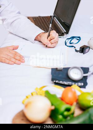 Hände des männlichen Ernährungswissenschaftlers, der sich Notizen an seinem Schreibtisch macht, Hände des Ernährungswissenschaftlers, die medizinische Aufzeichnungen in der Praxis machen. Nahaufnahme des Ernährungsschreibens Stockfoto