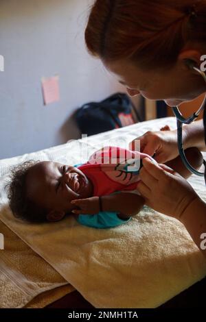 Ein weißer Arzt untersucht ein schwarzes Baby mit einem Stethoskop. Stockfoto