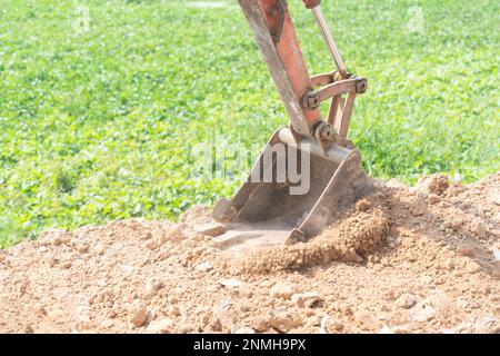 Nahaufnahme eines Mini-Grabschaufels, der den Boden auf einer Baustelle aushubt. Stockfoto
