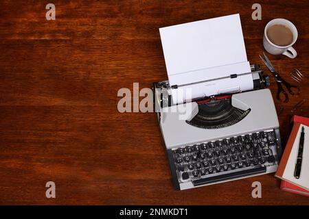 Eine flache Draufsicht auf eine Schreibmaschine aus den frühen 60er Jahren auf einem dunkelbraunen Schreibtisch, mit Büchern, Füllfederhalter und Kaffeetasse und Kopierbereich auf der linken Seite Stockfoto