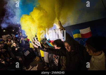 Die Demonstranten halten während des anti-kriegs-protestmarsches in Warschau blaue und gelbe Rauchfackeln. Tausende Polen, Ukrainer und Belarussen haben sich am Jahrestag des Angriffs vor der russischen Botschaft in Warschau versammelt, um gegen Russlands Aggression gegen die Ukraine zu protestieren und Solidarität mit der Ukraine zu zeigen. Demonstranten hielten ihre nationale Flagge und auch Schilder mit den geschriebenen Namen der im Krieg gefallenen Ukrainer. Die Menge marschierte später ins parlament, um Druck auf die weitere Unterstützung der Ukraine und die Verurteilung des Krieges auszuüben. Stockfoto