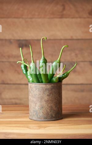 Grüne Chilischoten in einem alten rostigen Becher oder Behälter, gewöhnliches Gemüse für ihren würzigen Geschmack, auf einem Holztisch mit Platz zum Kopieren Stockfoto