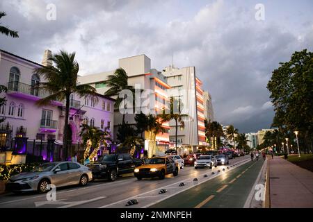 Abendfoto auf dem Ocean Drive im Viertel South Beach mit Menschen, die Rad fahren und laufen, während die Gebäude beleuchtet werden. Stockfoto