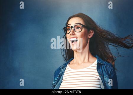 Das gibt's doch nicht. Studiofoto einer jungen Frau, die vor blauem Hintergrund Luft ins Gesicht geblasen hat. Stockfoto