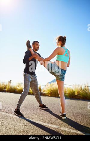 Wir unterstützen uns gegenseitig bei der Suche nach einem gesünderen Lebensstil. Ein sportliches junges Paar, das sich vor dem Laufen draußen dehnt. Stockfoto