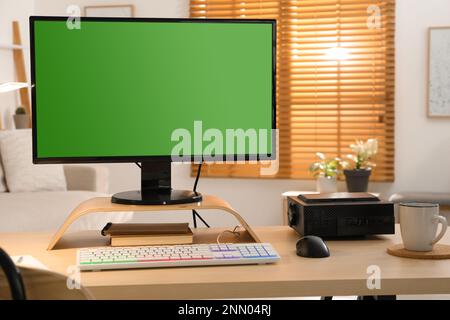 Moderner Computer und RGB-Tastatur auf Holztisch im Innenbereich. Grüner Bildschirm für Modellerstellung Stockfoto