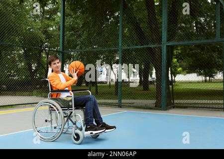 Behinderter Teenager im Rollstuhl, der Basketball auf dem Spielfeld spielt Stockfoto