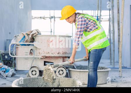 asiatische Arbeiterin, die als Arbeiterin auf der Baustelle hart arbeitet, mischt Betonzement von Hand Stockfoto