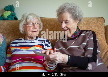 Zwei ältere Frauen im Alter von 90s Jahren, die lebenslange Freunde sind, sitzen zusammen, schauen sich ein Foto an und plaudern über die alten Zeiten. Stockfoto