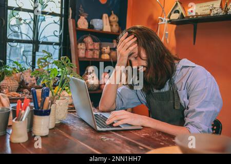 Künstler, der im Studio arbeitet, kein Kundenkontakt, Geschäft scheitert. Mann, Kopfschmerzen, erschöpft. Stockfoto