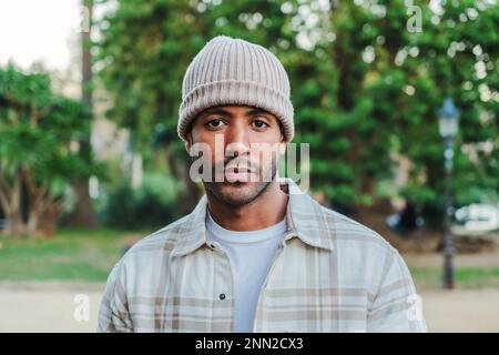 Nahaufnahme eines jungen, attraktiven afroamerikanischen Mannes mit Mütze, der vor der Kamera ernst aussieht. Von vorne sieht man einen hispanic, der draußen in einem Park mit trauriger Einstellung steht. Hochwertiges Foto Stockfoto