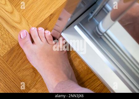 Frau schlug mit dem kleinen Zeh auf die Möbel. Zwischenfall zu Hause. Verletzung des kleinen Fingers des Fußes Stockfoto