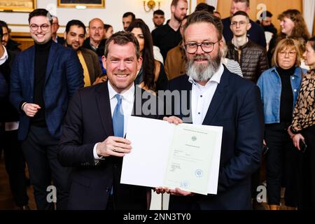 Kiel, Deutschland. 25. Februar 2023. Claus Ruhe Madsen (r, Independent), Schleswig-Holsteins Minister für Wirtschaft, Verkehr, Arbeit, Technologie und Tourismus, legt sein Einbürgerungszertifikat neben Ulf Kämpfer, Oberbürgermeister der Stadt Kiel, vor. Madsen, eine dänische Eingeborene, wurde im stadtrat von Kiels Rathaus eingebürgert. In der Hauptstadt des Bundesstaates wurden 2022 781 Menschen eingebürgert. Kredit: Frank Molter/dpa/Alamy Live News Stockfoto