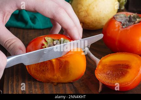 Scheiben frischer Persimonen auf dunklem Holzhintergrund, selektiver Fokus. Hände mit Messer. Diät und Vitamin Fresh. Ernte. Herbststillleben von frischem k Stockfoto