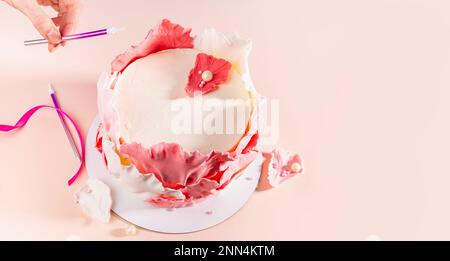 baker fügt Kerze zu festlichem Kuchen hinzu, selektiver Fokus, Kopierraum. Nahaufnahme der menschlichen Hand mit pinkfarbener Kerze im Vordergrund. Damendekoration auf Ca Stockfoto