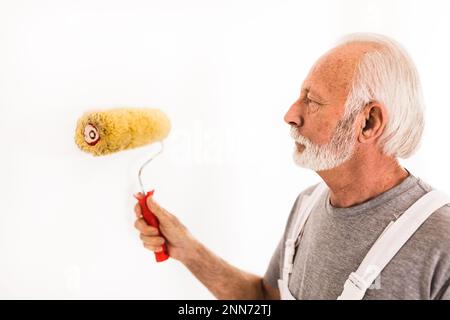 Senior-Arbeiter, der weiße Wände mit Roller malt Stockfoto