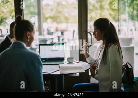 Drei Studenten sitzen und plaudern in einer Café-Bar über das neueste bevorstehende Projekt Stockfoto