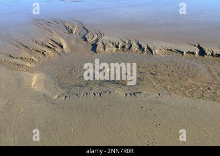 Ein Punkt im Sand, an dem eine natürliche Quelle aus Süßwasser bei Ebbe aufsteigt und der Sand wie Miniaturvulkane sprudelt. Stockfoto