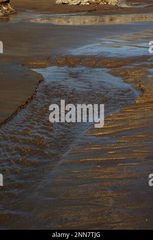 Ein Punkt im Sand, an dem eine natürliche Quelle aus Süßwasser bei Ebbe aufsteigt und der Sand wie Miniaturvulkane sprudelt. Stockfoto