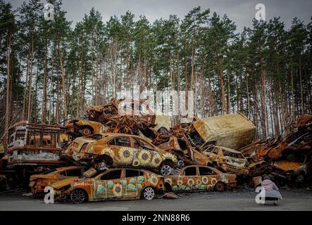 Irpin, Ukraine. 25. Februar 2023. Zerstörte Autos sind gestapelt und mit Sonnenblumen bemalt auf einer Hauptstraße von Irpin bei Kiew. Die Autos wurden hier zu Beginn des Krieges zerstört, als Russland vor etwa einem Jahr die Ukraine Angriff. Kredit: Kay Nietfeld/dpa/Alamy Live News Stockfoto