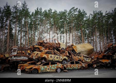 Irpin, Ukraine. 25. Februar 2023. Zerstörte Autos sind gestapelt und mit Sonnenblumen bemalt auf einer Hauptstraße von Irpin bei Kiew. Die Autos wurden hier zu Beginn des Krieges zerstört, als Russland vor etwa einem Jahr die Ukraine Angriff. Kredit: Kay Nietfeld/dpa/Alamy Live News Stockfoto