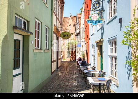 Gäste essen im Freien in einem Restaurant in einer engen Kopfsteinpflasterstraße im historischen Schnoor Quarte im Stadtzentrum von Bremen zu Mittag Stockfoto