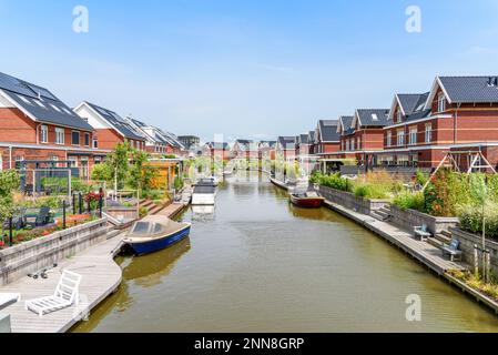 Moderne energieeffiziente Ziegelhäuser mit Sonnenkollektoren auf dem Dach entlang eines Kanals in den Niederlanden an einem sonnigen Sommertag Stockfoto