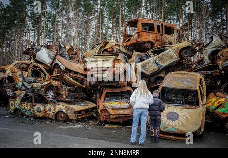 Irpin, Ukraine. 25. Februar 2023. Zerstörte Autos sind gestapelt und mit Sonnenblumen bemalt auf einer Hauptstraße von Irpin bei Kiew. Die Autos wurden hier zu Beginn des Krieges zerstört, als Russland vor etwa einem Jahr die Ukraine Angriff. Kredit: Kay Nietfeld/dpa/Alamy Live News Stockfoto