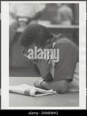 Das Foto zeigt einen jungen afroamerikanischen Mann mit Brille, der sich über eine Zeitung lehnt, New York, NY, 8/1956. (Foto von Angelo Rizzuto Stockfoto